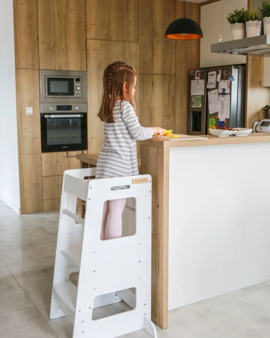 Petite fille sur une tour d'apprentissage KiddyMoon blanche dans une cuisine moderne