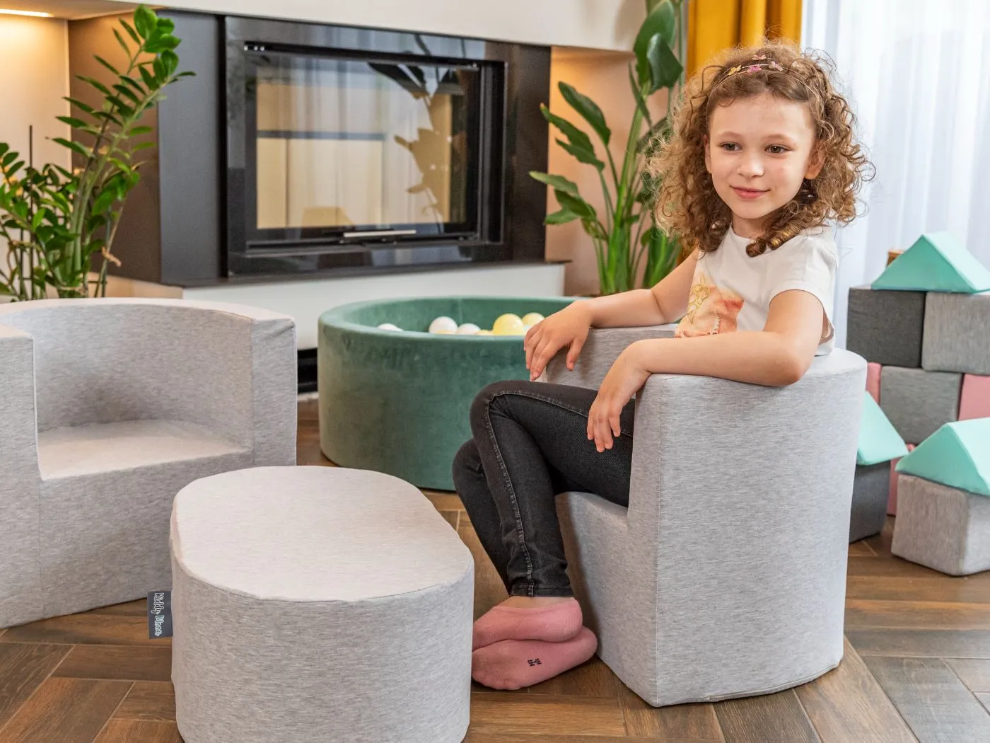 Petite fille assise sur un fauteuil en mousse gris avec son tabouret assorti dans un salon