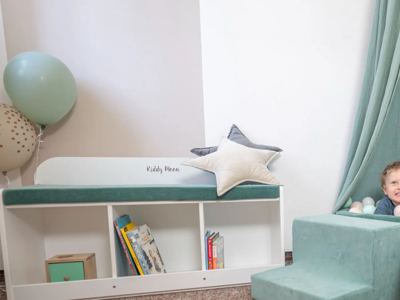 Banquette KiddyMoon blanche avec étagères ouvertes pour livres d'images et coussin vert sauge